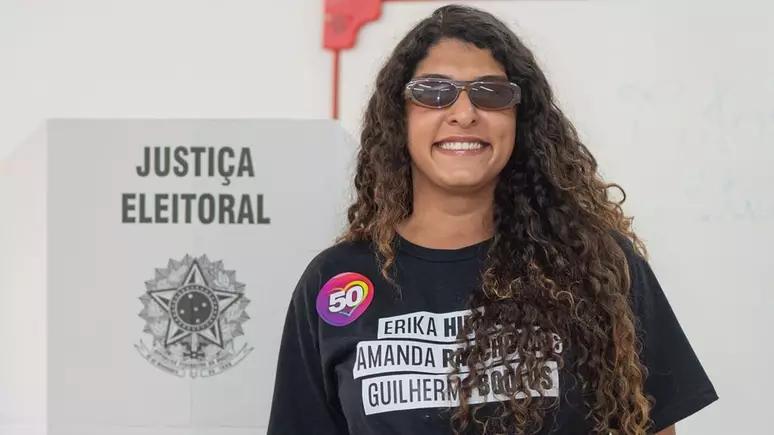 Pessoa usando óculos de sol em frente a uma urna de votação, pronta para exercer seu direito democrático